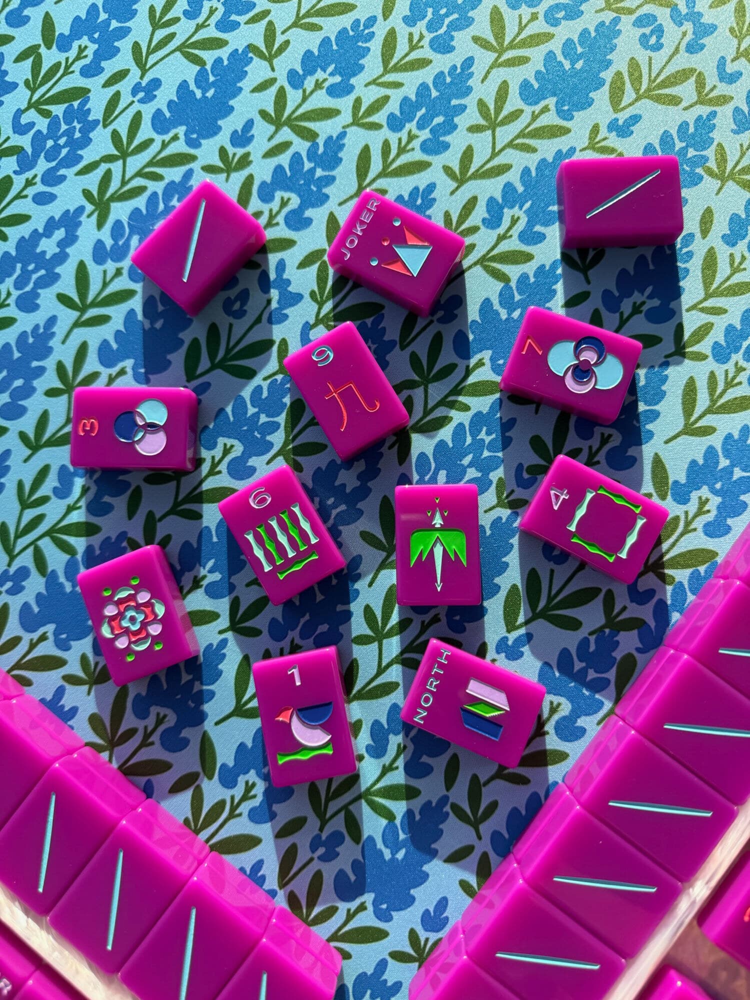 Magenta mahjong tiles casting long shadows on a blue and green floral mat
