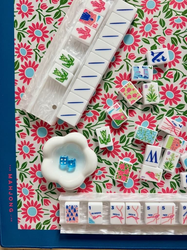 White mahjong tiles with pink and green designs on a floral mat
