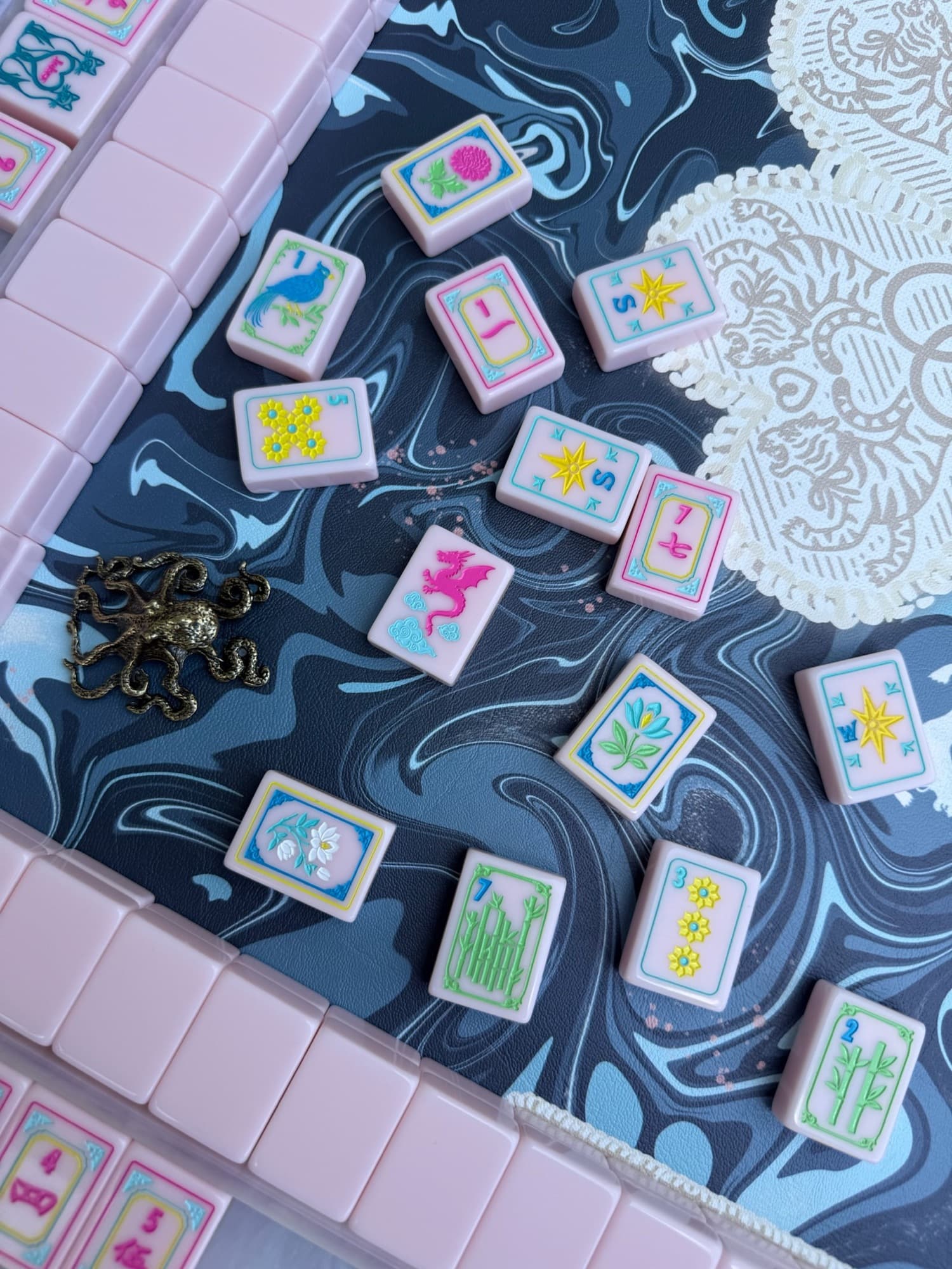 Pink mahjong tiles on a navy marbled mat with a brass octopus and a lace doily