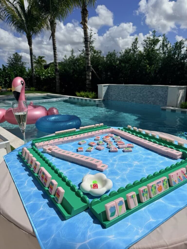 A poolside mahjong table with mint racks, a water print mat and a flamingo float